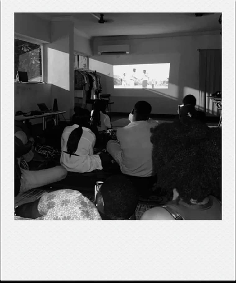 A film projected onto a wall while an audience watches from the floor.