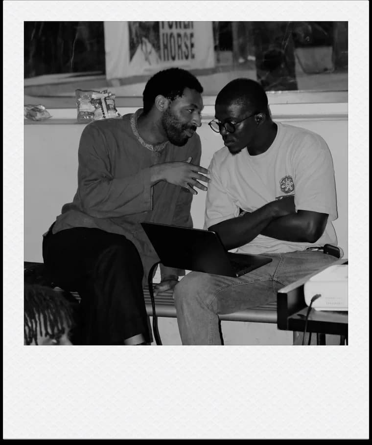 Two men sitting on a bench in conversation over an open laptop.